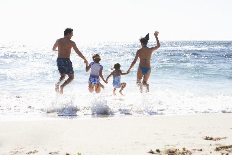 Two,Generation,Family,Wearing,Swimwear,,Jumping,Above,Surf,On,Sandy